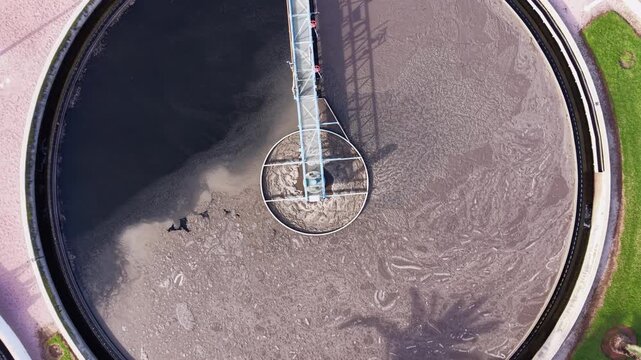 Top-down aerial view of a circular clarifier at a Spanish wastewater treatment plant as the camera rises, revealing rotating sludge patterns, mechanical arms, and clean industrial geometry
