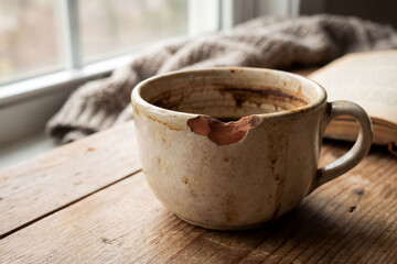 Broken cup on wooden table by window in afternoon light