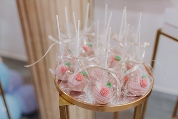 Pink cake pops decorated with tiny frosting roses and wrapped individually in clear plastic with ribbon, served on a round golden platter at a sweet table