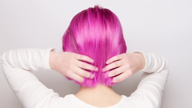 A woman against a white background shows off her pink hair. Hairstyle concept.