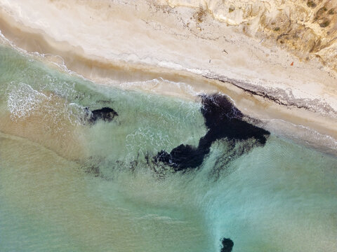 Aerial view of the turquoise sea gently meeting the sandy Firiplaka beach under the bright sun, a serene coastal scene., Firiplaka beach, Milos, Greece.
