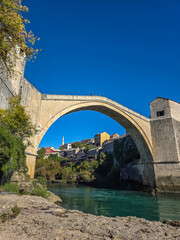 Naklejka premium The iconic stone arch of Stari Most rising above the turquoise Neretva River with the old town of Mostar in the background.