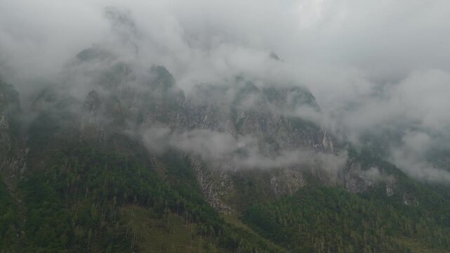 Aerial drone flying forward along mountain walls with low hanging clouds and fog on peaks Italy