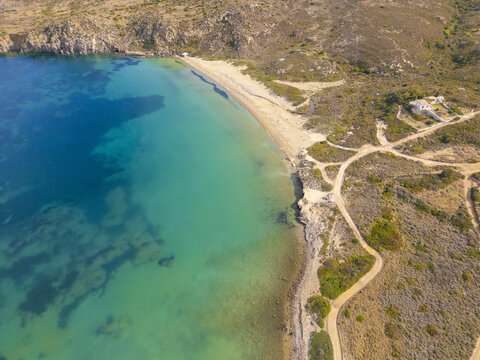 Aerial view of turquoise waters meeting the sandy beach, contrasting with the rugged coastline and sparse vegetation, Rivari Lagoon, Milos, Greece.
