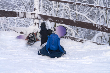 Losing her balance on the ski slope. A snowboarder in a playful blue helmet lies in the snow near a wooden fence with snow-covered trees in the background.