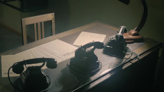 In the semi-darkness there is an old-fashioned Soviet-era table with a lamp, newspapers and black, gloomy rotary telephones. Closeup. Shot in motion
