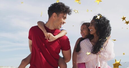 Obraz premium Smiling family standing close together at beach, wearing red T-shirt and pink blouse, gold stars