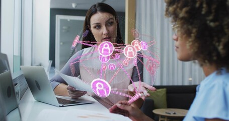 Pointing dark-haired woman in light blouse holding papers explaining pink AR network at office desk