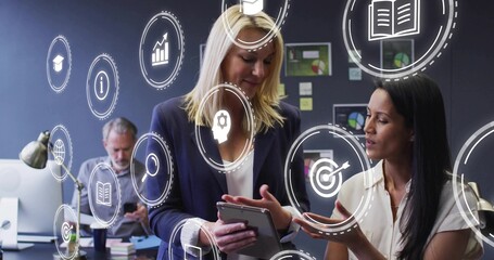 Collaborating two women in navy blazer and blouse, reviewing tablet in office with HUD icons