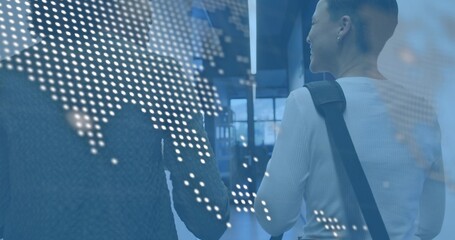 Walking two women with bag strap and darker sweater through modern lobby, dotted world map overlay