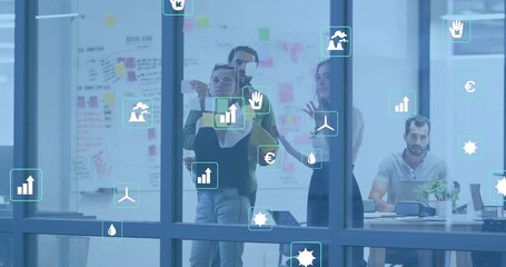 Working team of four in business casual arranging sticky notes on glass in office with laptop