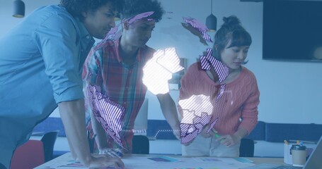 Leaning three adults reviewing printed charts in modern meeting room, with projected globe overlay