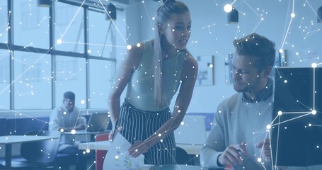 Leaning colleague in sleeveless top, holding charts at monitor in open office with digital overlay