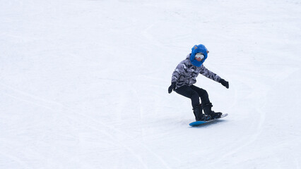 A lone figure of a teenage snowboarder on a ski slope. Copy space.