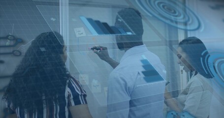 Writing man in blue shirt holding marker, marking glass wall at office, sticky notes, data overlay