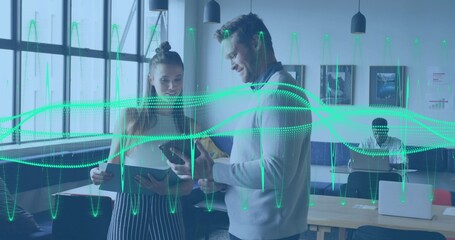 Talking pair in light sweater and sleeveless top viewing tablet and phone in office, green waveform