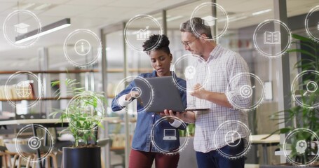 Pointing man in checked shirt while woman in denim holding laptop at modern office, showing icons