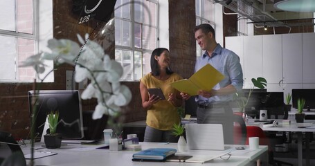 Reviewing files, team in open office in blue shirt and mustard top, holding yellow folder, tablet