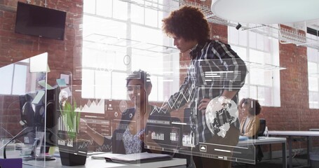 Leaning man in dark plaid shirt pointing at monitors in loft office, showing HUD overlays