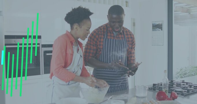Mixing couple wearing aprons stirring batter in bright modern home kitchen, with smartphone nearby - Powered by Adobe