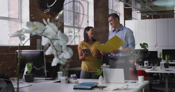 Reviewing files, team in open office in blue shirt and mustard top, holding yellow folder, tablet