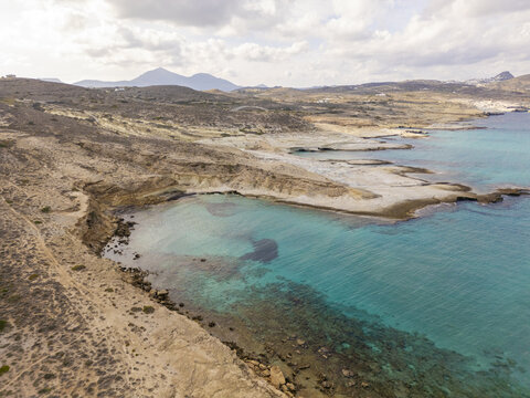 Aerial view of turquoise waters gently embrace the rugged coastline near the cliffs, showcasing the stark contrast between sea and land, Paralia Mitikas, Milos, Greece.