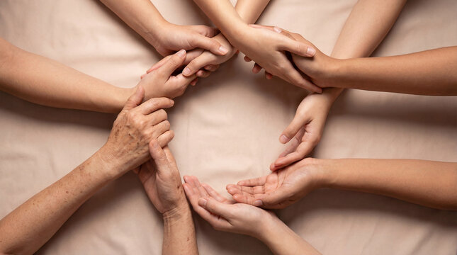 Top view of hands of multi generational women joining together in a circle on beige fabric