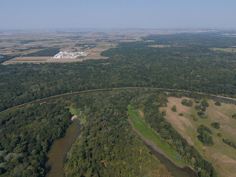 Aerial view of the Morava River's oxbow lake, a tapestry of green forests meeting golden fields under a hazy sky, Vysoka pri Morave, Bratislava Region, Slovakia.