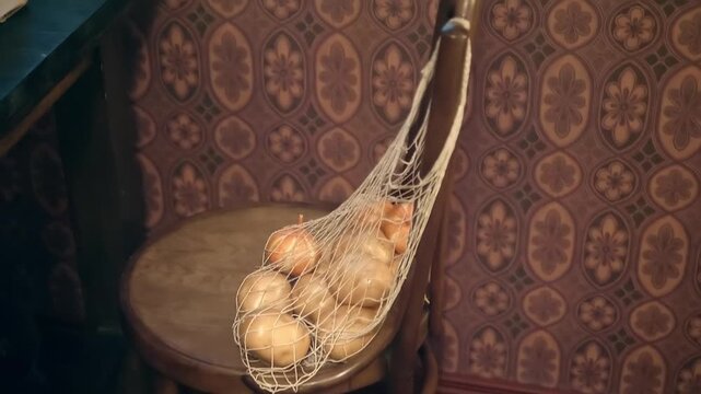 A mesh bag containing onions, freshly bought from the store, is hung on the back of a obsolete chair. Closeup. Shot in motion