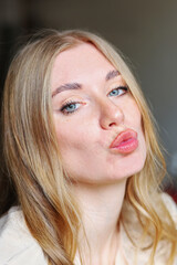 Naklejka premium Playful close up portrait of young woman with natural makeup blowing a kiss showing expressive lips soft skin and friendly emotional mood suitable for beauty lifestyle and social media concepts