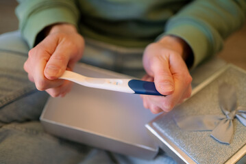 Person's hands holding a positive pregnancy test stick open from a silver gift box, symbolizing a life-changing announcement of becoming new parents and celebrating future parenthood