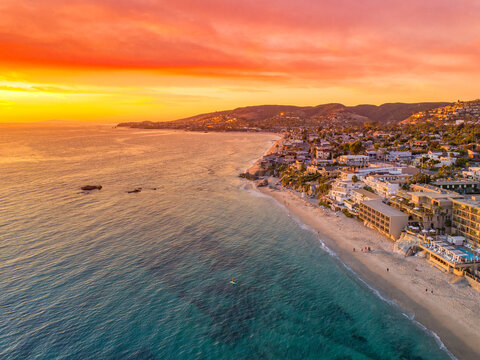 Aerial view of the coastline where the sky explodes in fiery hues over the tranquil ocean waters and sandy beaches, Laguna Beach, California, United States.