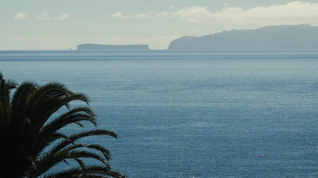 A telephoto shot of the distant silhouette of the Desertas Islands, captured from the parking area of Madeira Airport. The remote islands appear on the horizon approximately 35 kilometers away