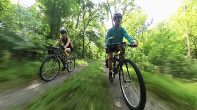 Mature couple rides bikes on dirt path beside C and O Canal in Maryland near the Potomac River during a sunny day.