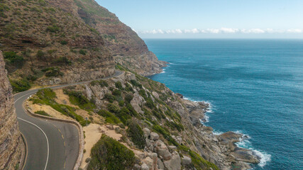 Aerial view of Chapmans Peak Drive winds, a ribbon of asphalt clinging to the rugged cliffs above the turquoise Atlantic, Cape Town, Western Cape, South Africa.