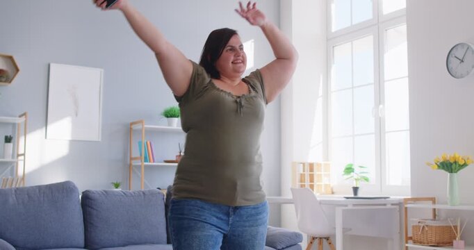 Joyful and happy woman has fun at home, dancing and relaxing to music during domestic leisure time. She enjoys the holiday atmosphere, celebrating freedom with happiness and chill vibes.