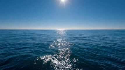 Fototapeta premium A vast expanse of deep blue ocean meets a clear blue sky with the sun casting a brilliant shimmering reflection on the water s surface