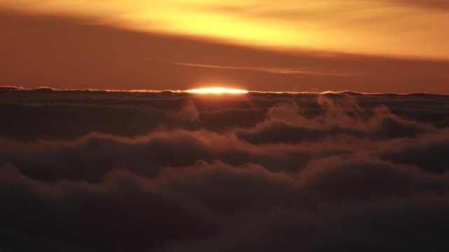 A telephoto time-lapse video showing clouds moving across the sky while the last edges of the sun disappear behind them in Madeira. Warm sunset light filters through the clouds, creating a dramatic