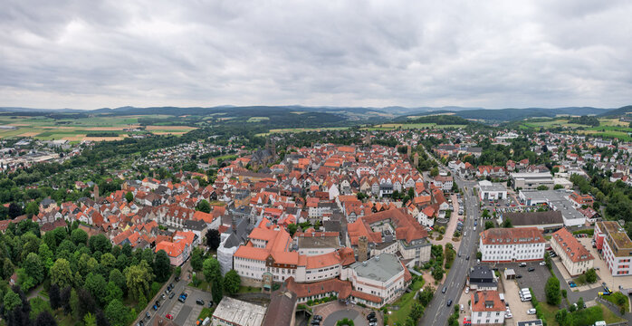 Aerial view of a quaint town with red-tiled roofs nestled amidst lush greenery under a cloudy sky, Bad Hersfeld, Hessen, Germany.