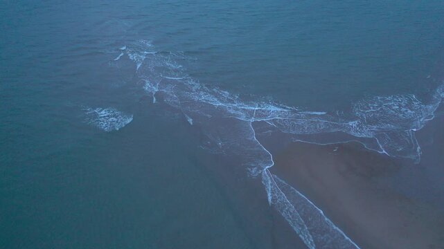 Aerial view of tide waves meeting on a sandy shore in Teriberka. Calm but moody Arctic seascape with blue water and foam on the Kola Peninsula coast, Russia