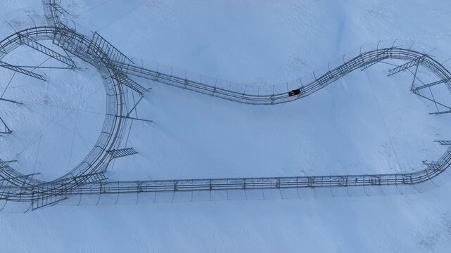 Drone view of a bobsled mountain coaster winding through the snow-covered Caucasus mountains in Bakuriani resort, featuring people enjoying the winter attraction.