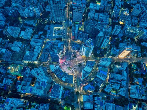 Aerial view of a bustling cityscape with towering buildings and a circular road pattern illuminated in the twilight glow, Dhaka, Dhaka Division, Bangladesh.
