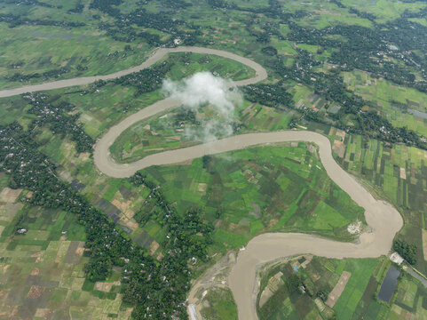 Aerial view of the snaking river carving through the lush green landscape, a cloud hovering above, Manikganj, Dhaka Division, Bangladesh.