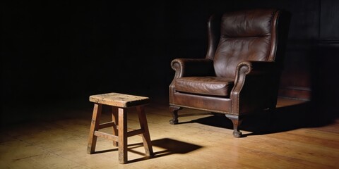 Vintage leather armchair and rustic wooden stool in dramatic spotlight