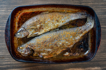 Delicious baked two trout fish with spices in a glass baking dish, closeup, top view