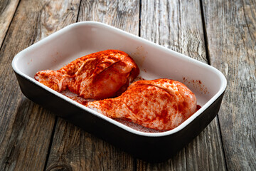 Raw seasoned chicken drumsticks in baking dish on wooden table	