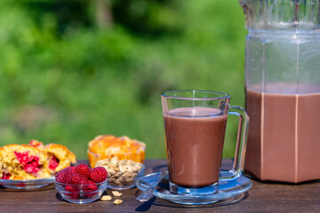Indian masala chai or tea or cacao in glass with jug and raspberry muffin on the table in cafe on nature background, close up. Trendy healthy drink