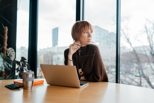 White woman aged 40 looking away while working on laptop at office table