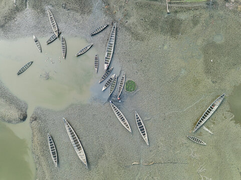 Aerial view of rustic wooden boats scattered on the muddy banks of the river, a stark tableau of desolation, Kishoreganj, Dhaka Division, Bangladesh.