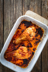 Baked chicken drumsticks in baking dish on wooden table. Top view